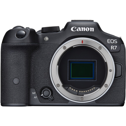 A Canon EOS R7 mirrorless camera with a black body and a mounted lens, placed on a flat surface, showcasing its sleek design and professional features.