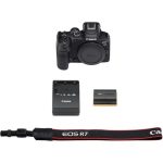 A Canon EOS R7 mirrorless camera with a black body and a mounted lens, placed on a flat surface, showcasing its sleek design and professional features.