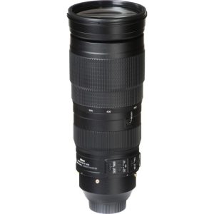 A close-up of the Nikon AF-S NIKKOR 200-500mm f/5.6E ED VR telephoto zoom lens, showcasing its large barrel, zoom ring, and gold 'NIKKOR' branding. The lens is mounted on a Nikon DSLR camera, ready for action photography.